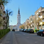 Kamienice na Rynku w Głubczycach z widoczną wieżą ratusza w tle. Ulica z parkującymi samochodami.