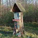 Przydrożna kapliczka w gminie Grodków, stojąca przy polnej drodze na tle pól i drzew