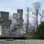 Pomnik ofiar represji stalinowskich w Brzegu, betonowa monumentalna konstrukcja z krzyżami i figurami ludzkimi, otoczona drzewami