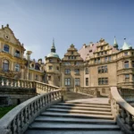 Monumentalne schody z balustradą prowadzące do zamku w Mosznej, z elewacją pałacu widoczną na tle nieba