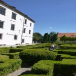 Zielony labirynt ogrodowy przy Zamku Piastów Śląskich w Brzegu, geometryczne żywopłoty z bukszpanu z widokiem na białe budynki zamkowe