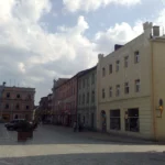 Kamienice przy rynku w Głuchołazach, w tym budynek Rynek 12, z zaparkowanymi samochodami przed fasadami