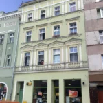 Kamienice przy rynku w Głuchołazach z zaparkowanymi samochodami przed fasadami