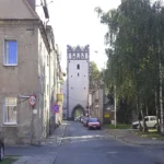 Ulica w Grodkowie prowadząca w stronę Bramy Ziębickiej, z kamienicami po obu stronach i wieżą bramną w tle