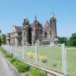 Panoramiczny widok zamku w Mosznej z rozległym trawnikiem i drzewami na pierwszym planie