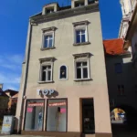 Kamienica przy Rynku 26 w Prudniku, widoczna od strony południowej, z odnowioną elewacją i witrynami w parterze