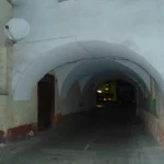 Nocne przejście pod kamienicą przy prudnickim Rynku z łukowymi podcieniami i oświetleniem ulicznym